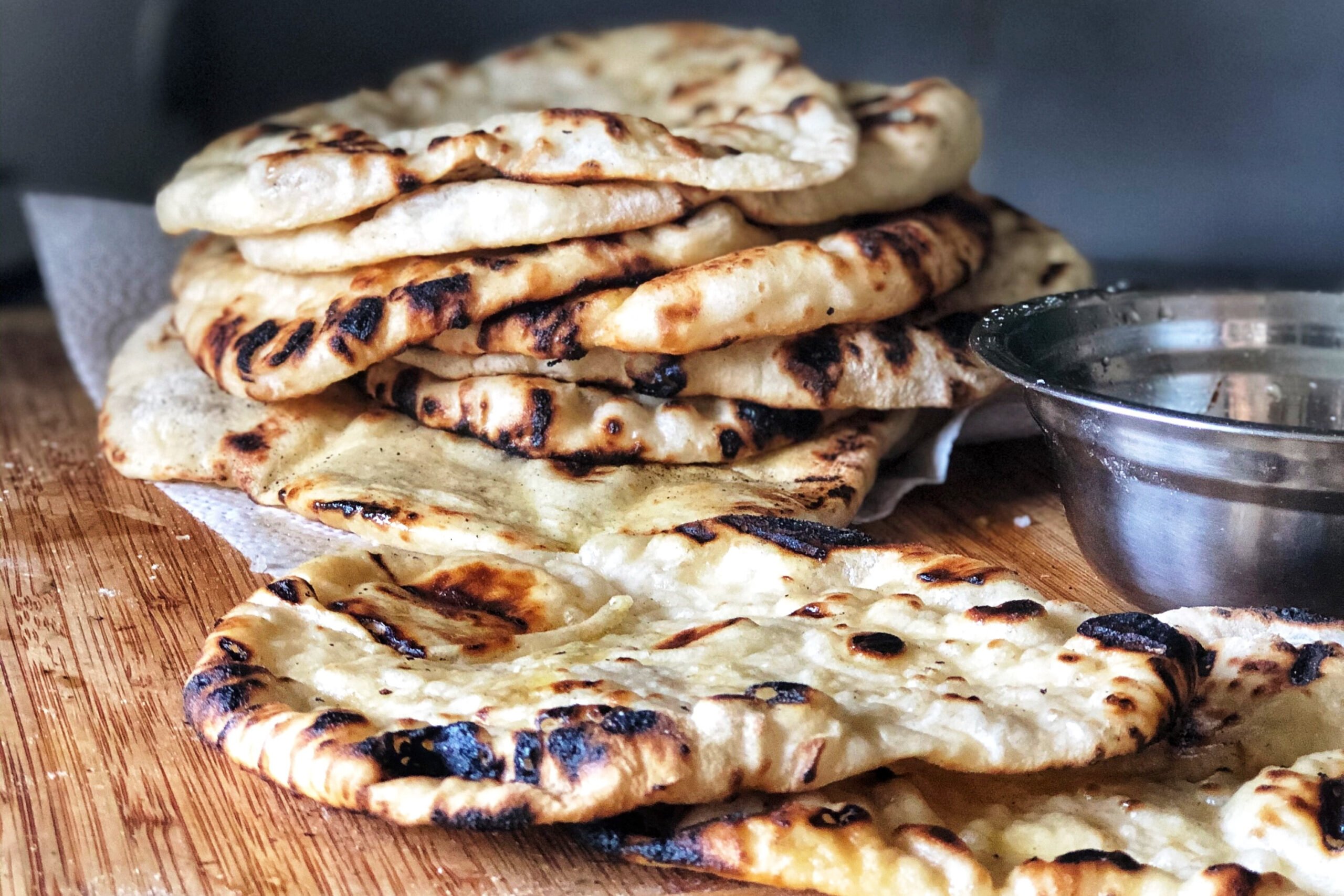 pile of flatbread on cutting board with silver bowl