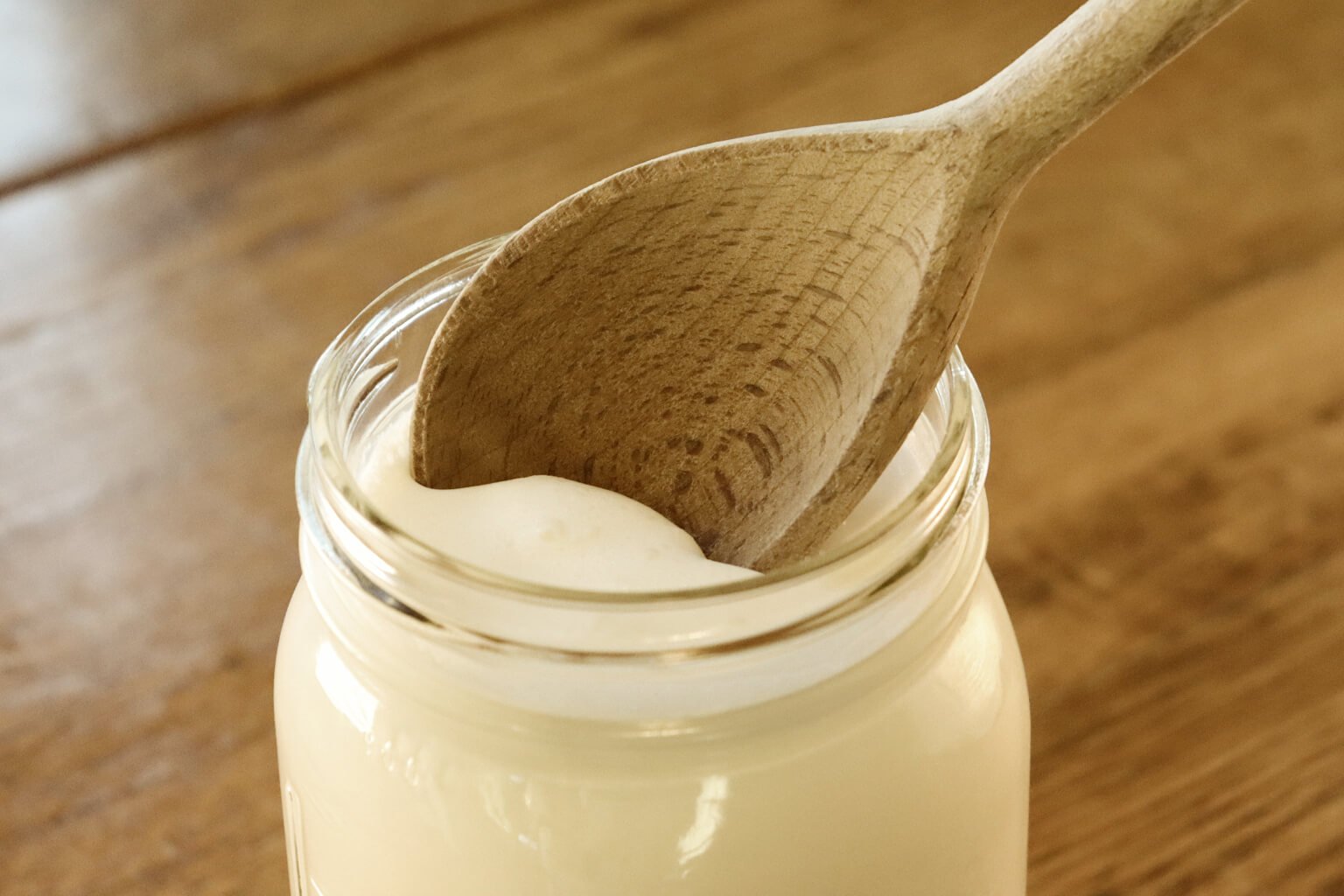 skimming cream off the top of a mason jar filled with milk using a wooden spoon