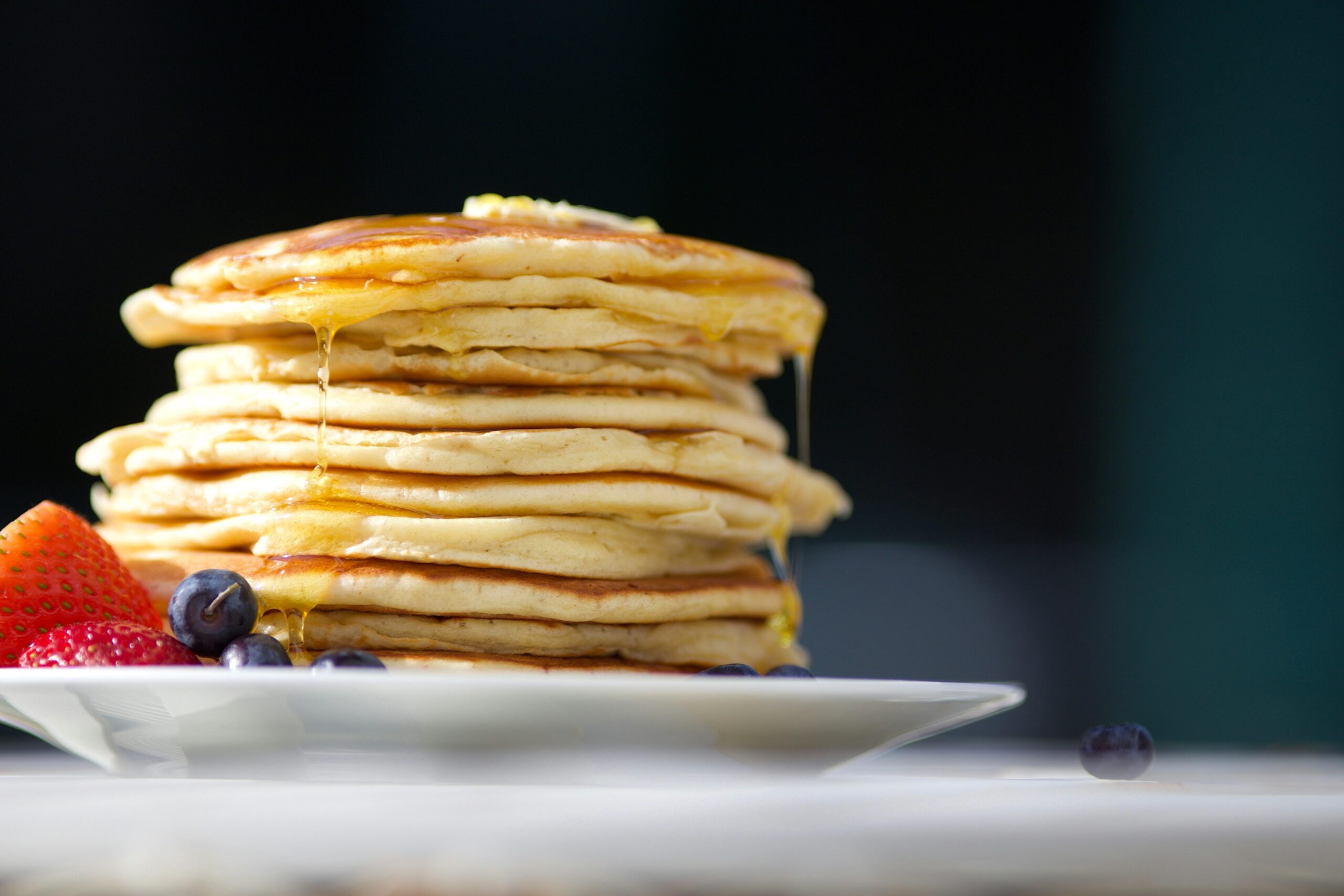 stack of pancakes with fruit, butter, and drizzled in maple syrup